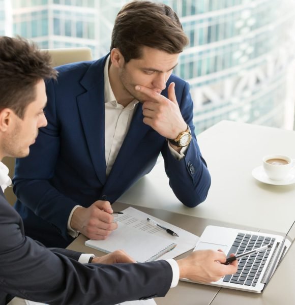 Business partners using laptop while working together on important corporate project in office. Businessman attentively listening to adviser Investment specialist making presentation of promising deal